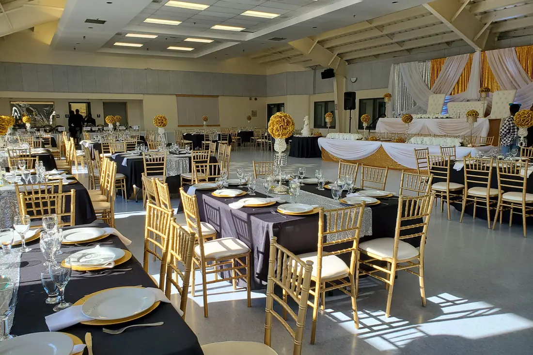 Black floor-length wedding linens with gold chiavari chairs and gold-rimmed place settings in a daylit banquet room