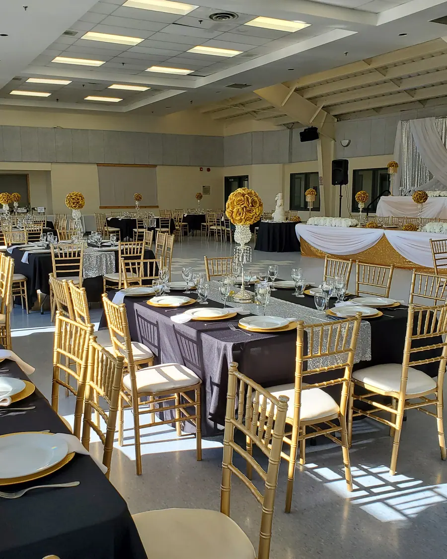 Black floor-length wedding linens with gold chiavari chairs and gold-rimmed place settings in a daylit banquet room