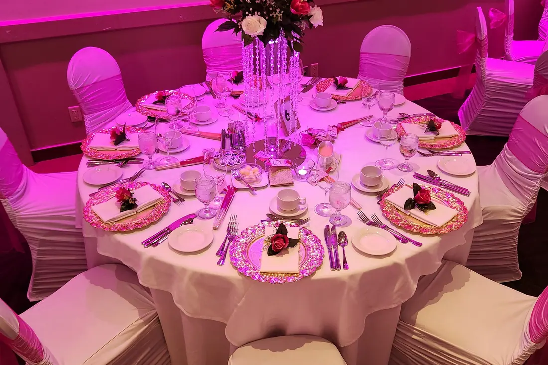 Blush and burgundy floral centerpiece on a crystal stand with pink charger plates under rose-pink uplighting