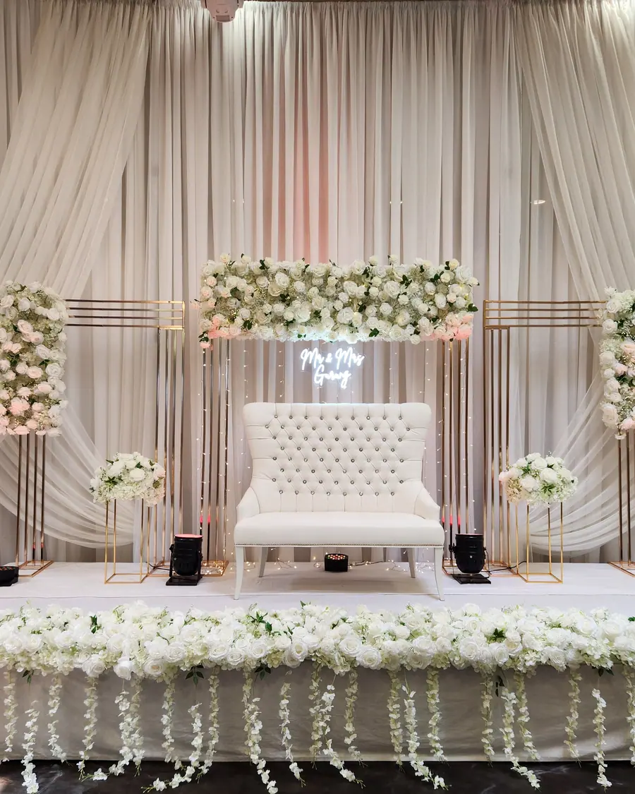 Blush and white floral columns framing a tufted loveseat, a custom neon sign and a sweetheart table draped in trailing greenery