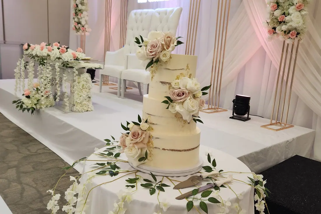 Four-tier semi-naked wedding cake dressed with blush roses and eucalyptus beside a floral head table