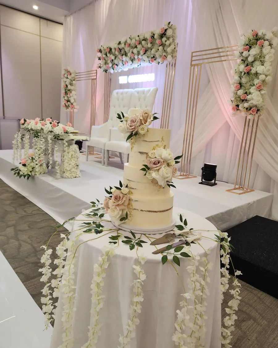 Four-tier semi-naked wedding cake dressed with blush roses and eucalyptus beside a floral head table