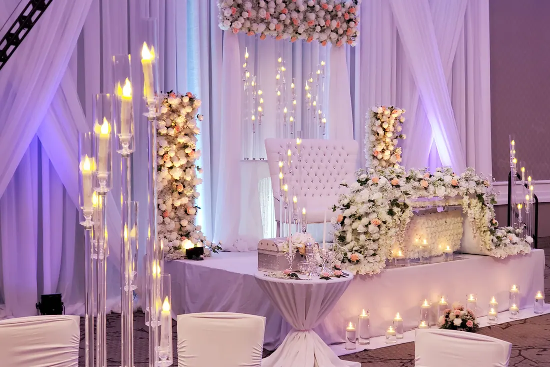 Ivory wedding head table with white roses, tall candelabras of pillar candles and a softly lit draped backdrop
