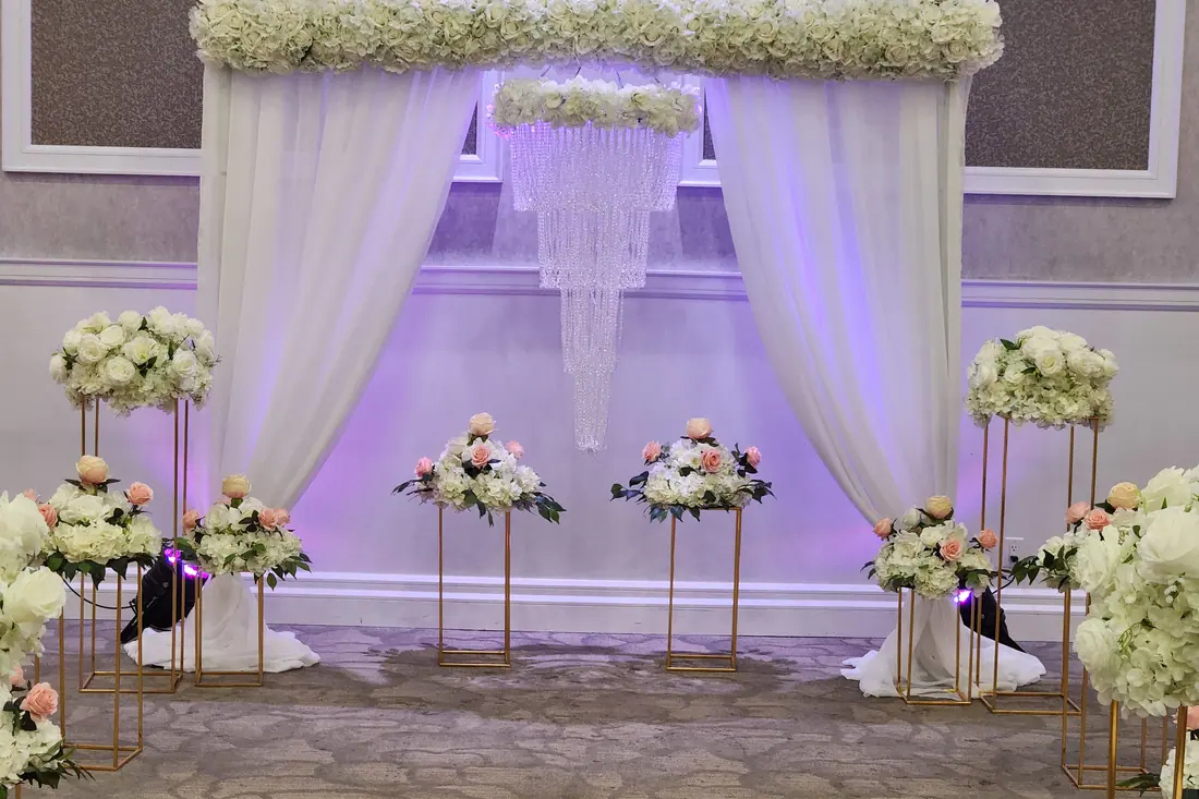 Ivory draped head table backdrop with a cascading crystal chandelier curtain and blush florals on tall gold stands