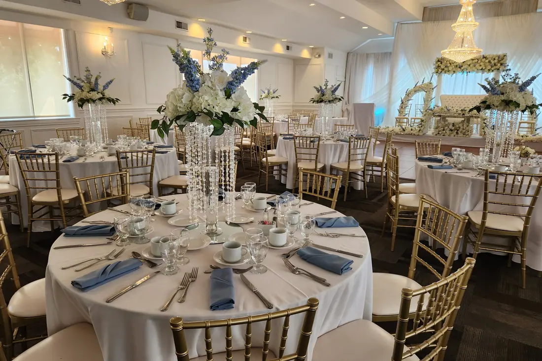 Dusty blue napkins and gold chiavari chairs around a crystal centerpiece of white and blue blooms in a classic ballroom