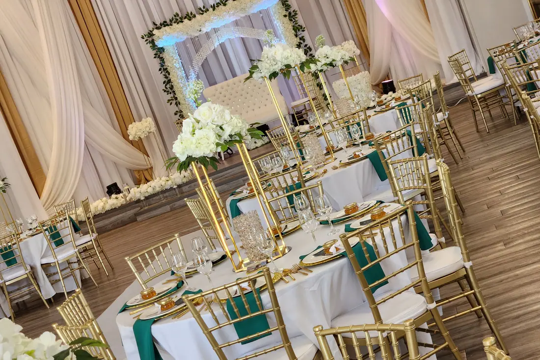 Emerald green wedding tablescape with gold chiavari chairs, gold chargers and towering gold floral stands in a draped ballroom