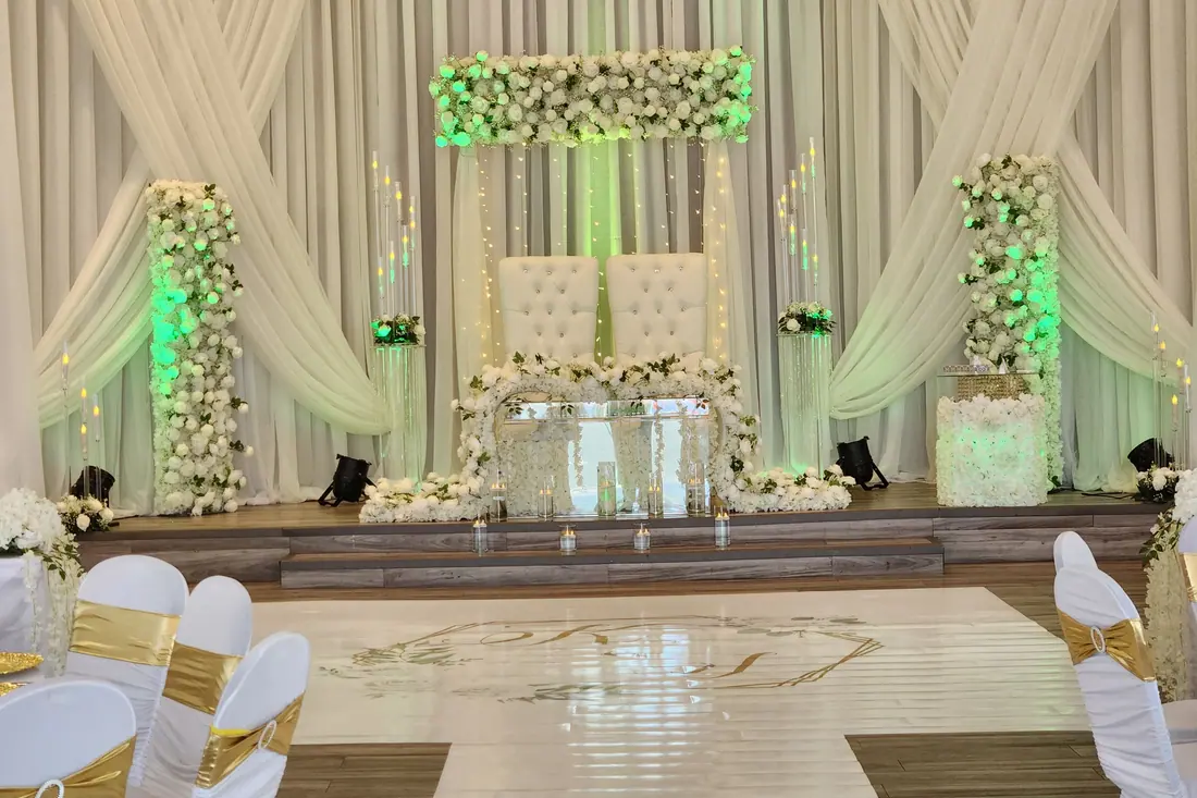 Ivory draped backdrop with white floral columns above a glossy custom monogram wedding dance floor wrap