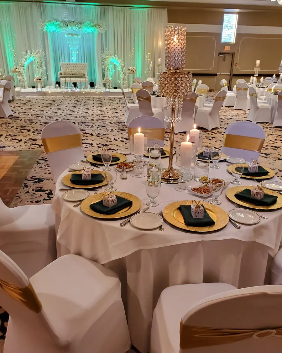 Close wedding place setting with gold charger plate, black napkin, gold favour box and a tall gold candelabra with pillar candles