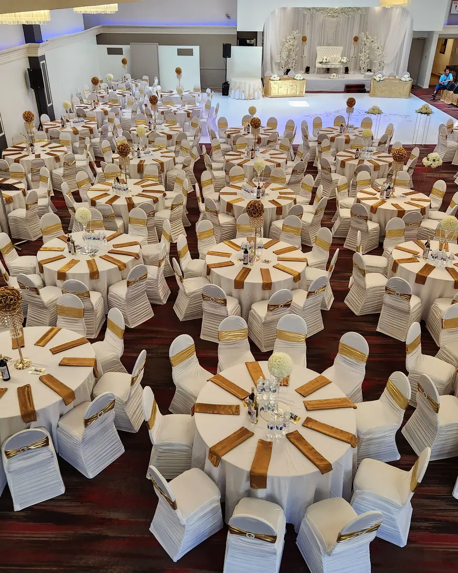 Full Ottawa wedding reception of dozens of round tables with white chair covers, gold sashes and gold floral pomanders