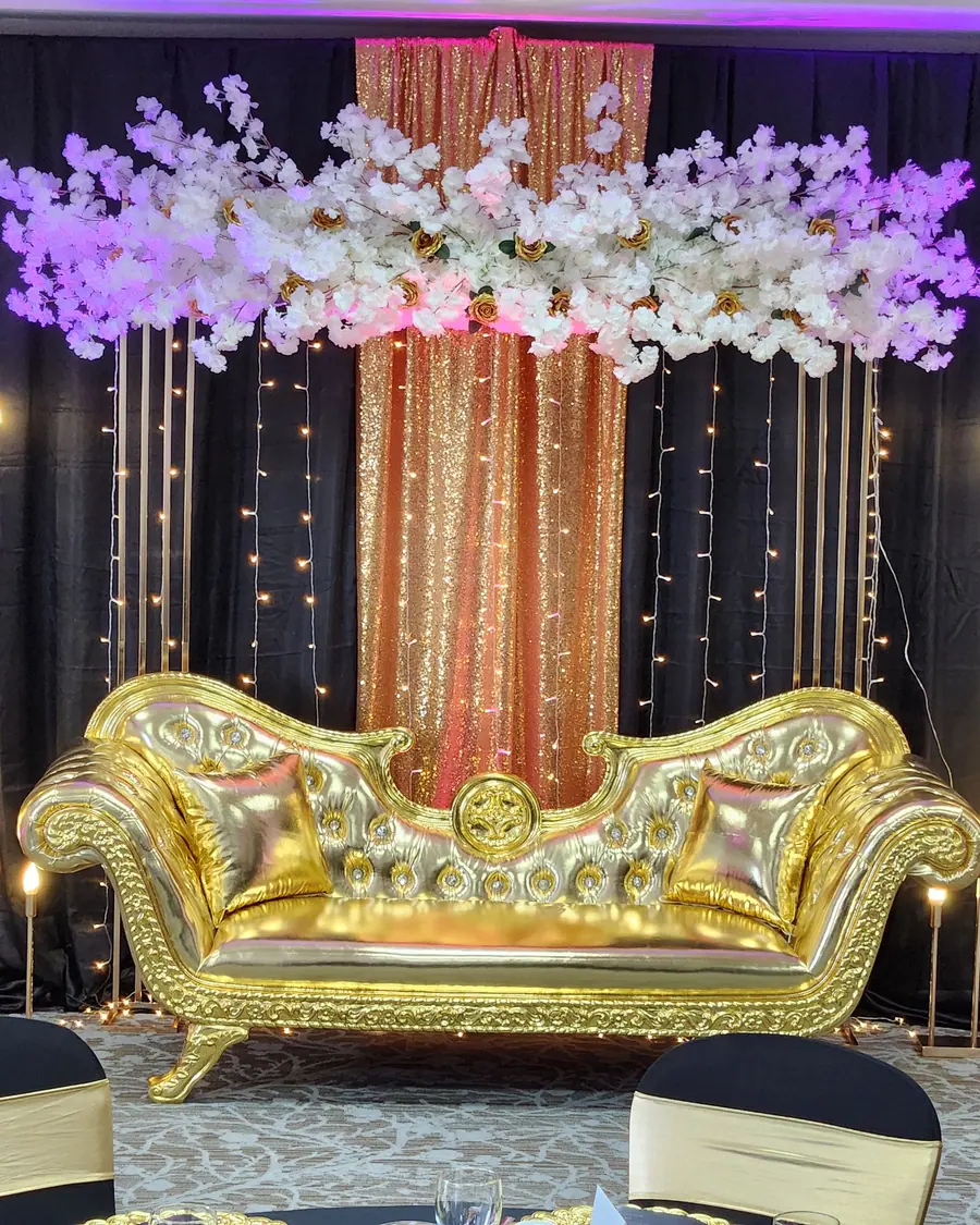 Dramatic black and rose gold sequin backdrop with a gold carved settee, cherry blossom canopy and a row of tall gold candlesticks