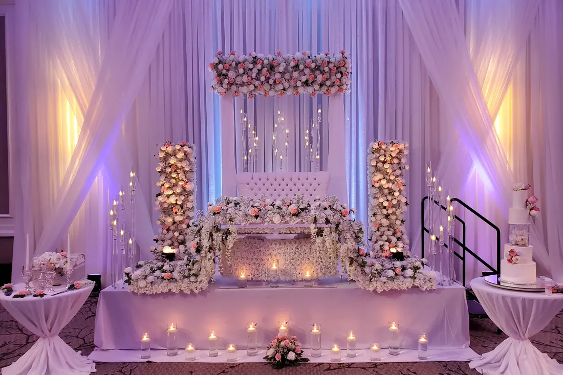 Lavender-lit ivory draped backdrop with blush floral columns, a hanging floral valance and a tiered wedding cake alongside