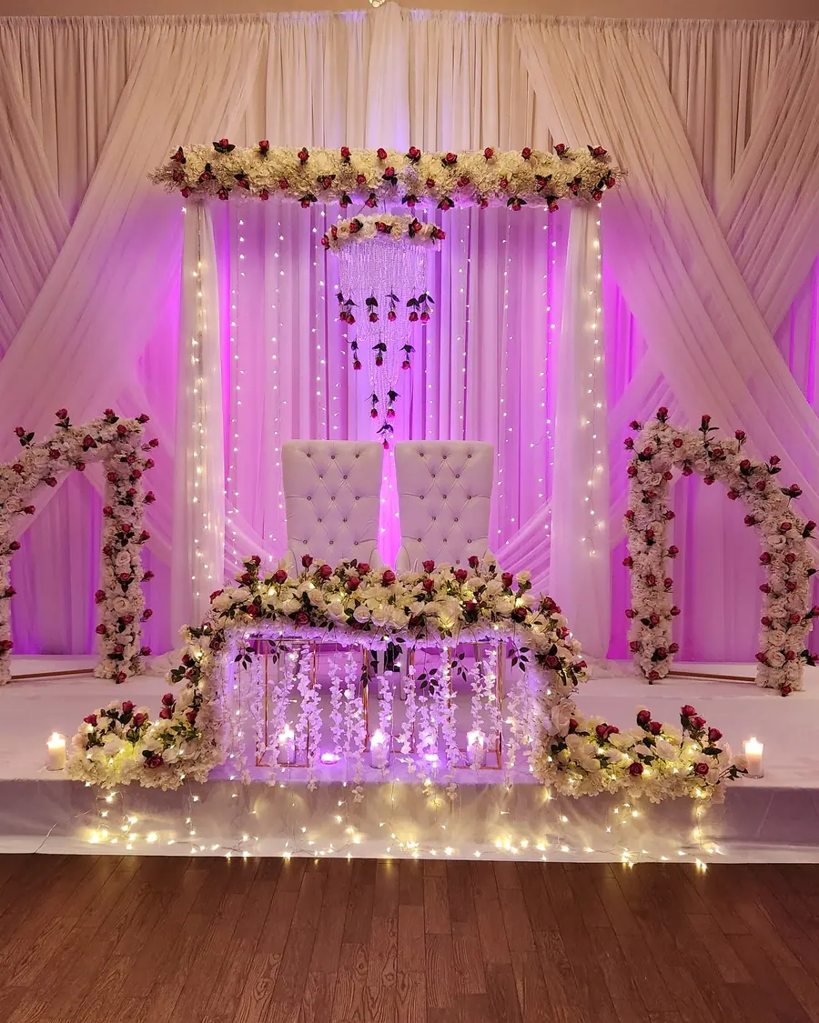 Wedding stage under magenta and pink uplighting with floral archways, fairy lights and a mirrored sweetheart table