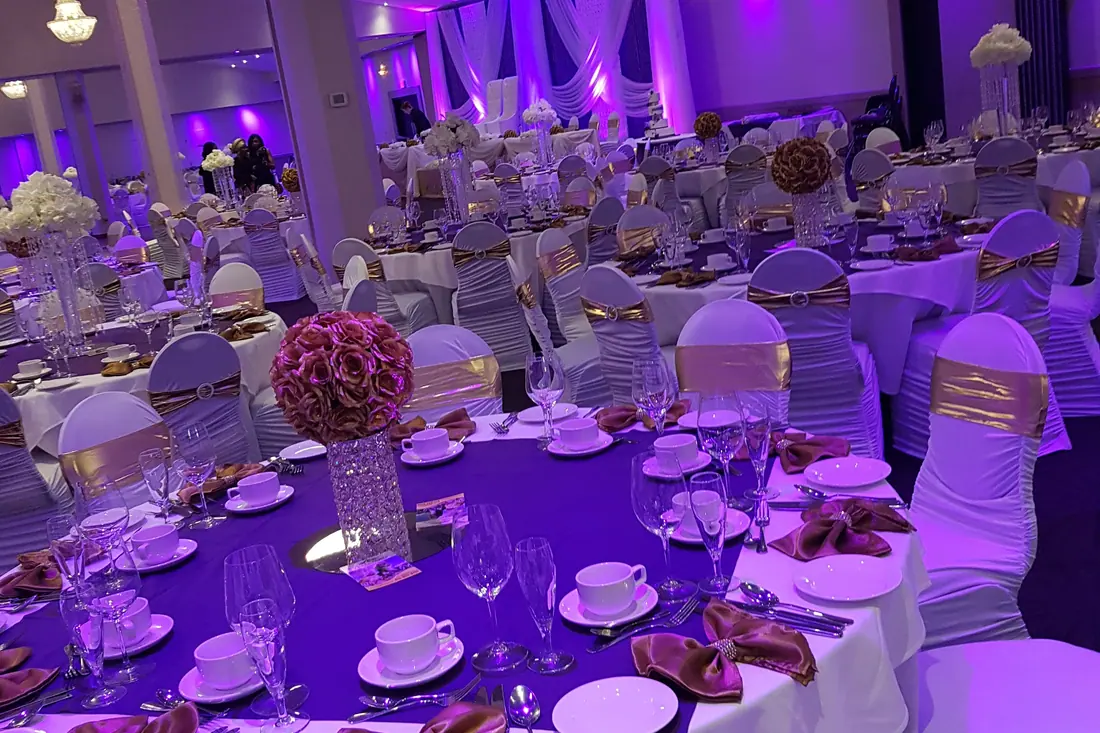 Magenta rose pomander centerpiece on a crystal stand above a white wedding table in a violet-lit reception hall