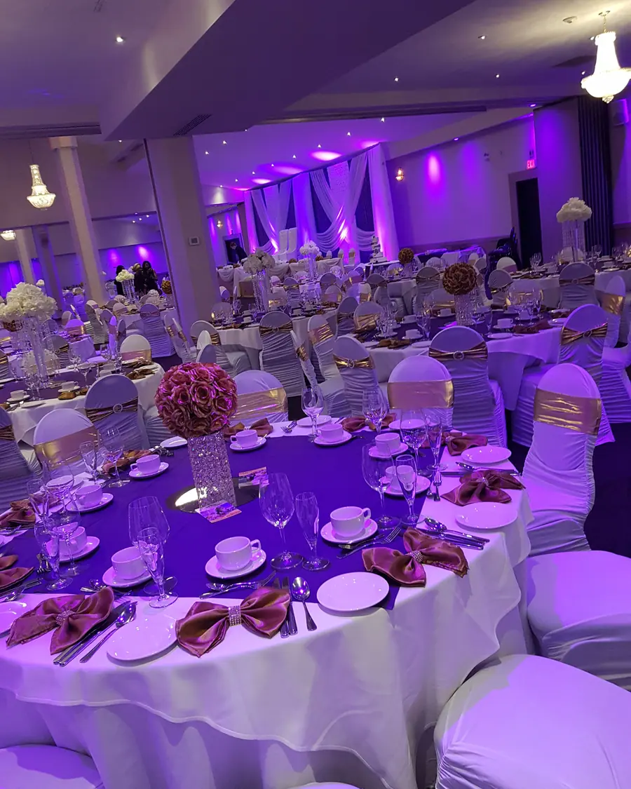 Magenta rose pomander centerpiece on a crystal stand above a white wedding table in a violet-lit reception hall