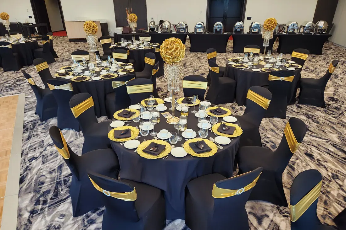 Navy blue floor-length linen with gold charger plates, gold chair sashes and a tall gold pedestal centerpiece of white blooms