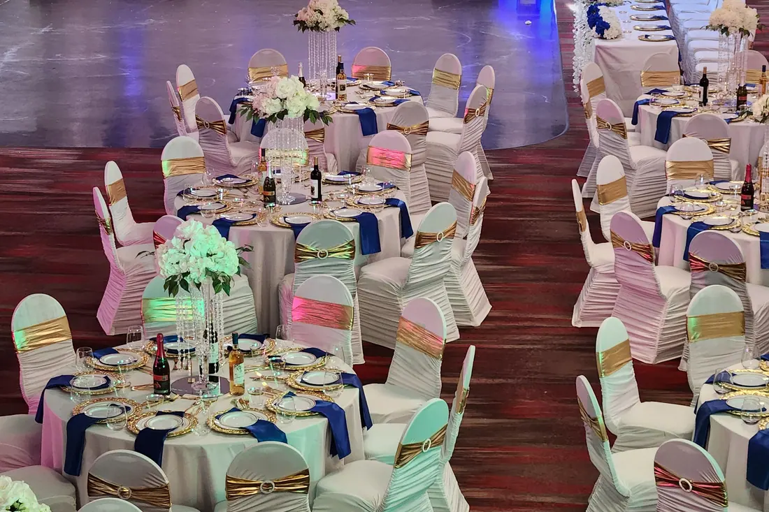 Long white banquet tables with navy blue napkins, gold charger plates and gold sashes on fitted white chair covers