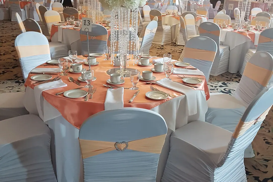 Peach satin table overlay with matching chair sashes on white fitted chair covers and a tall crystal centerpiece