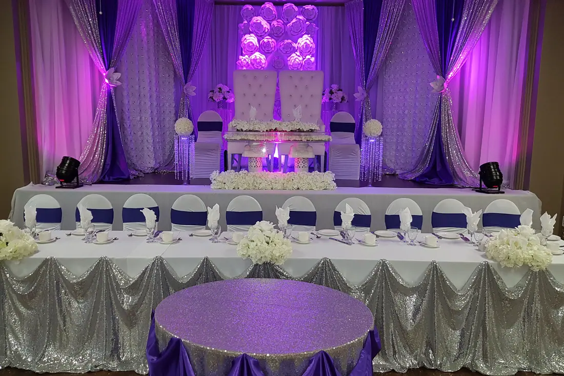 Long wedding head table with silver sequin skirting and white florals under deep purple and magenta ballroom uplighting