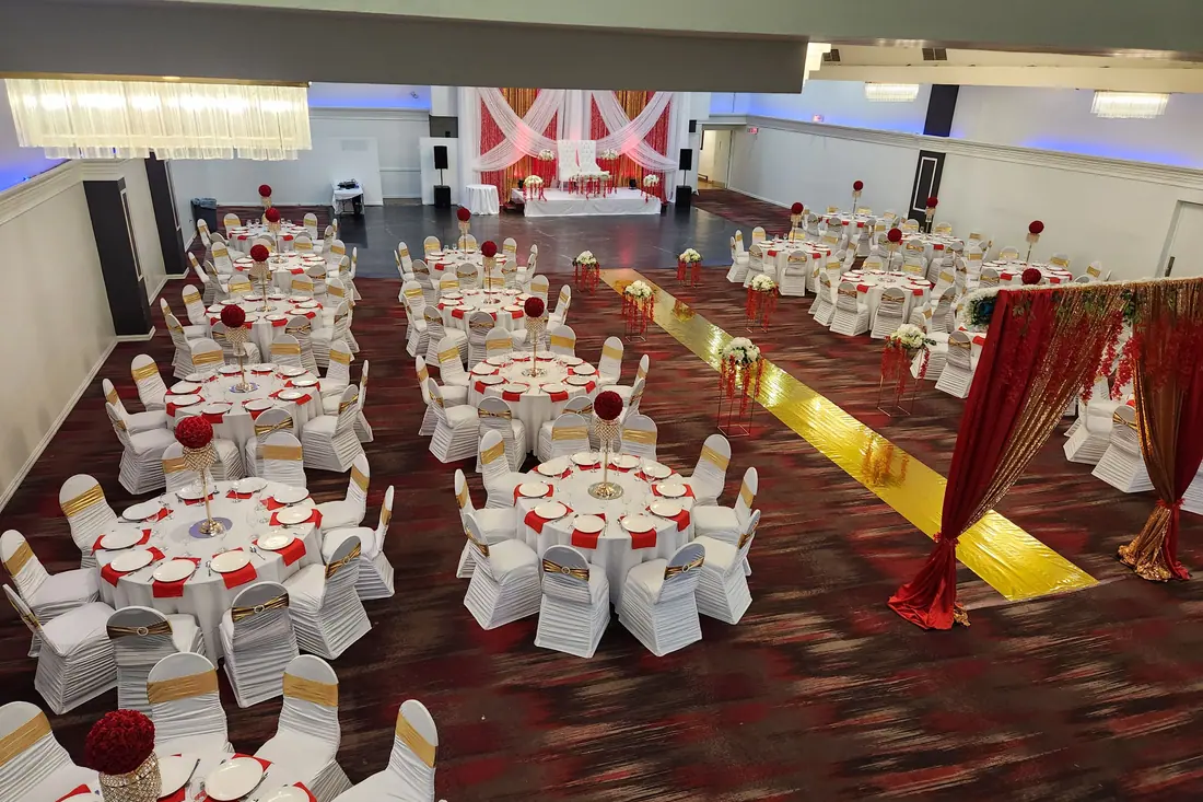Red and gold aisle runner leading through a reception of white covered chairs with red rose centerpieces