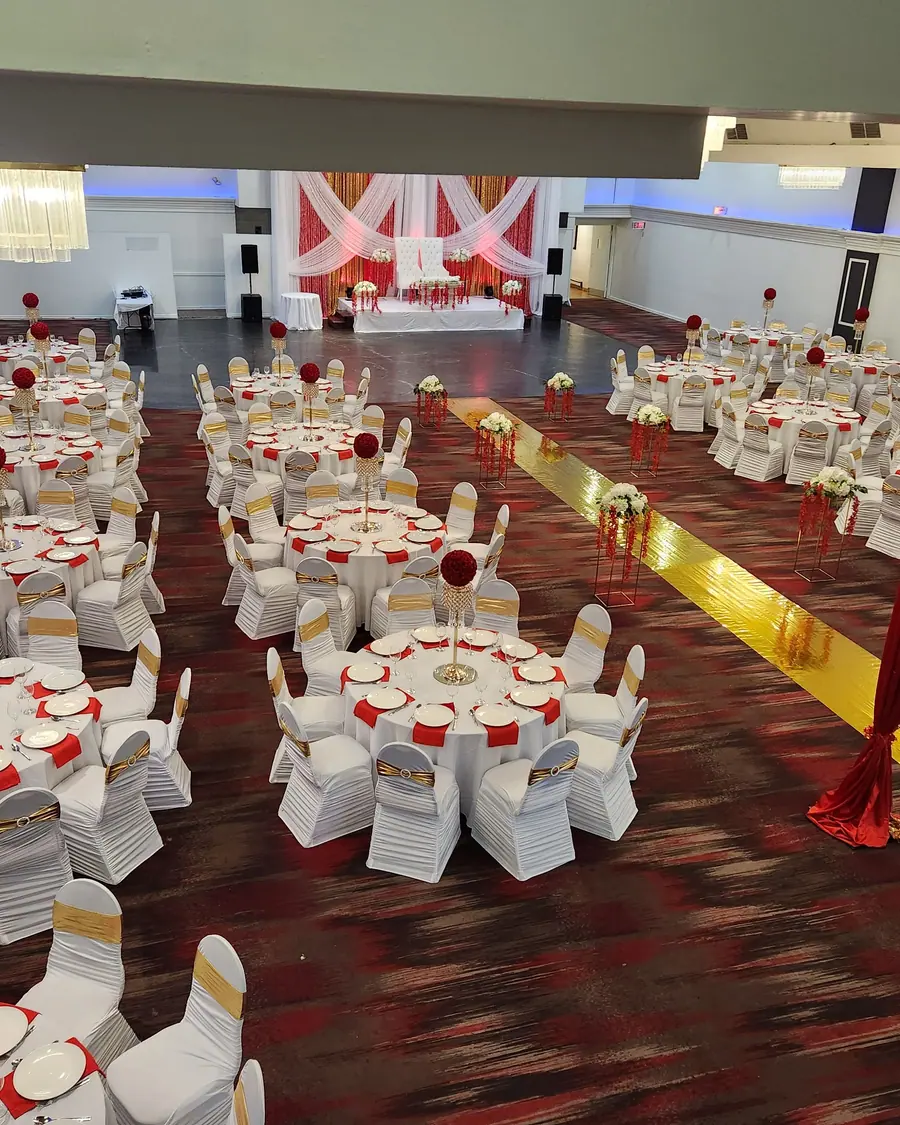 Red and gold aisle runner leading through a reception of white covered chairs with red rose centerpieces