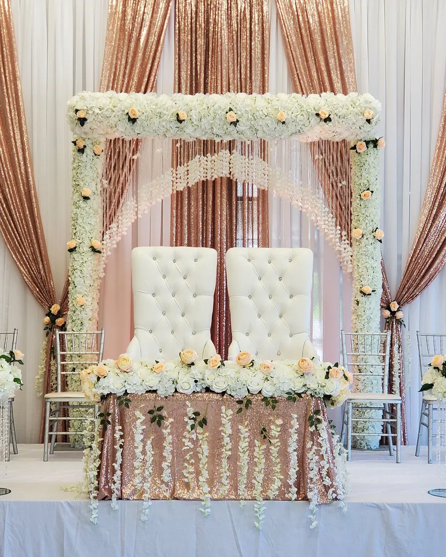 Rose gold sequin and ivory draped backdrop with a white floral canopy above a head table skirted in hanging blossoms