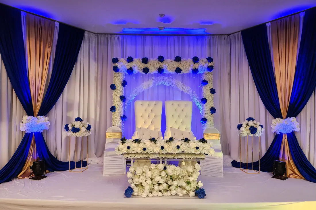 Royal blue and white wedding backdrop with navy side draping, blue and white floral panels and a pair of tufted chairs