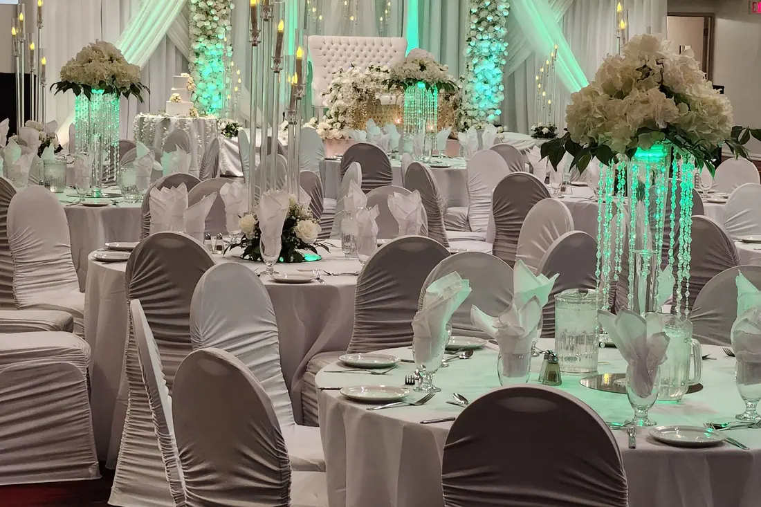 Tall crystal centerpieces with white blooms above silver-grey chair covers in a reception lit in turquoise
